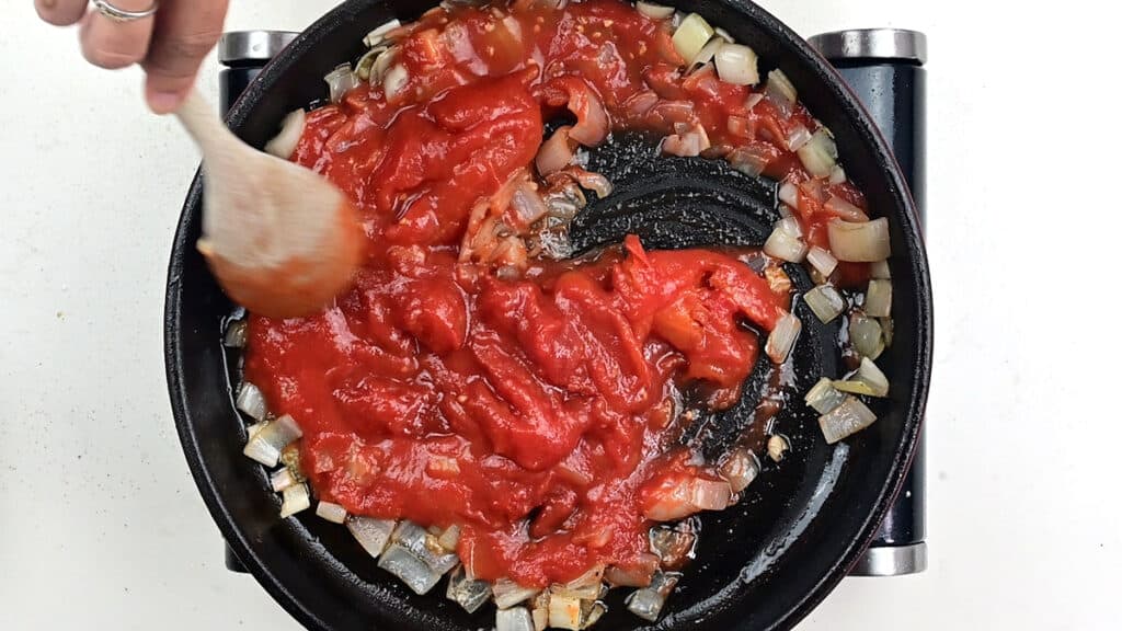 breaking up plum tomatoes with wooden spoon in skillet