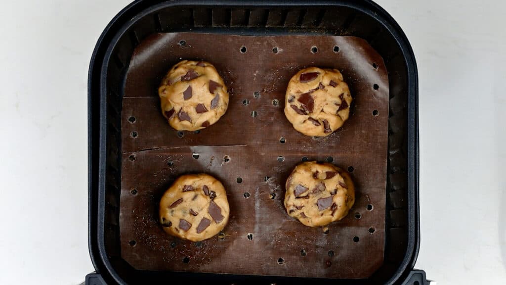 chocolate chip cookies in the basket of an air fryer before cooking 