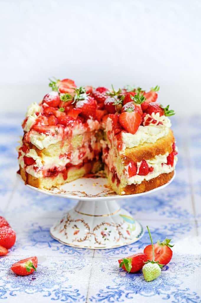 Strawberry shortcake cake on a cake stand with slice cut out