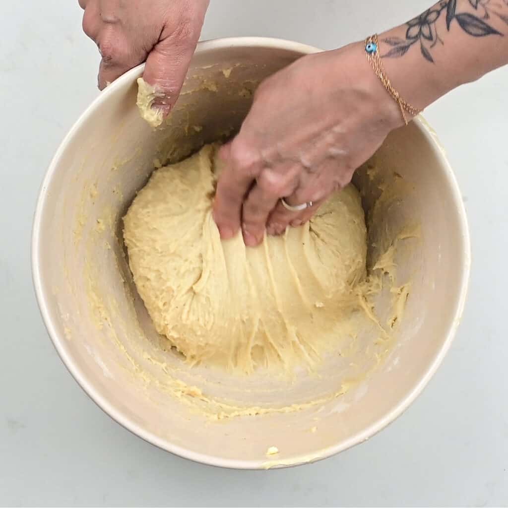stretching and folding doughnut dough in a mixing bowl