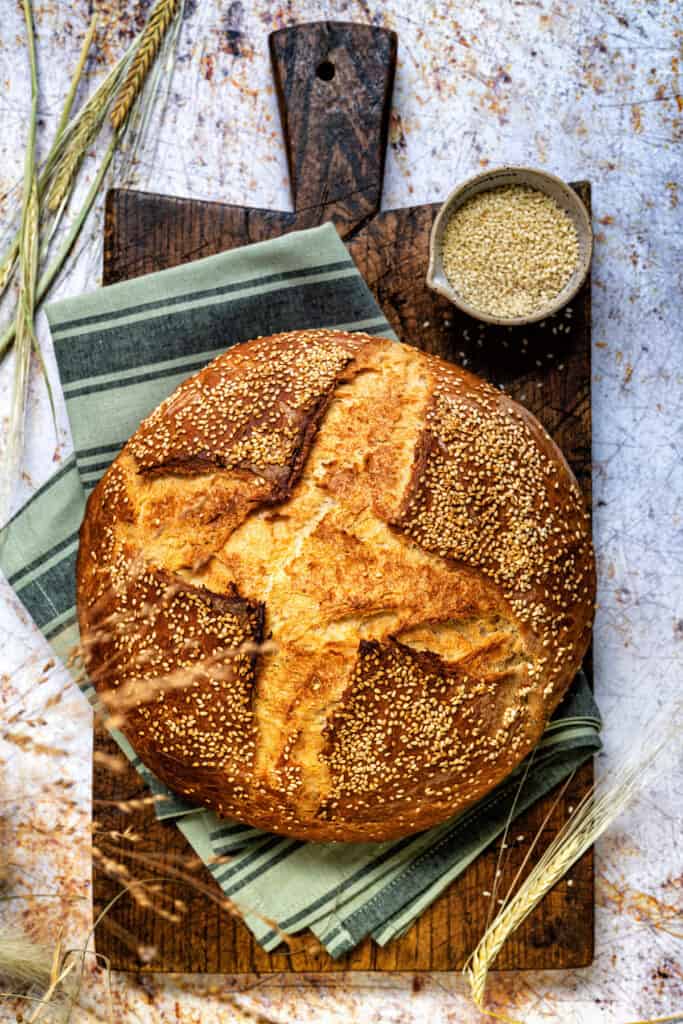 Greek Country Style Village bread topped with sesame seeds on a wooden board