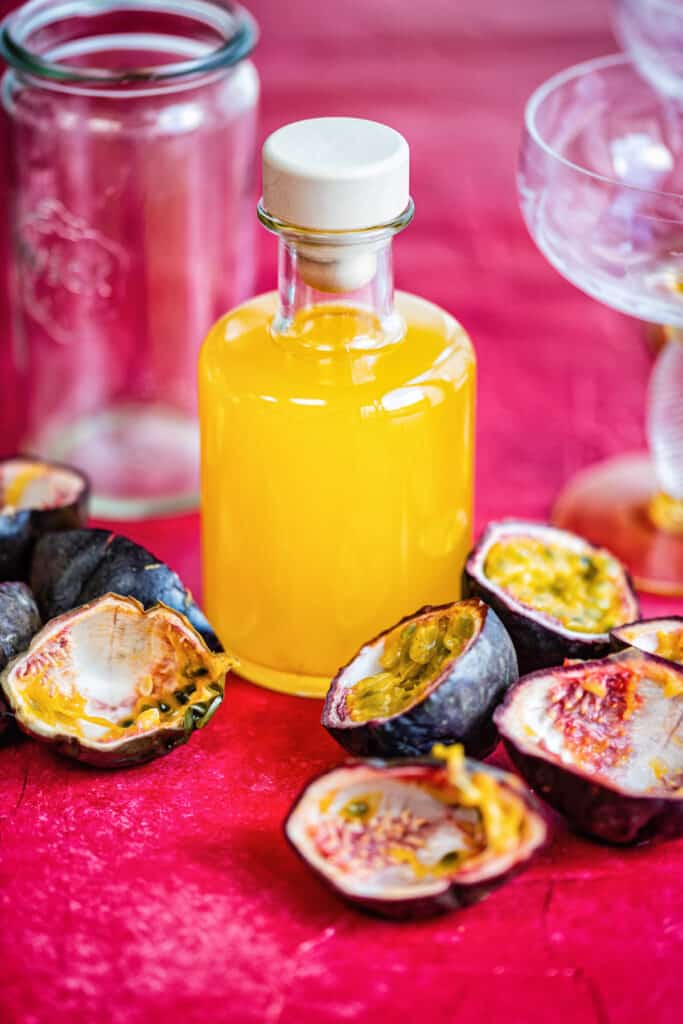 homemade passionfruit syrup in a small glass bottle with fruit on the side
