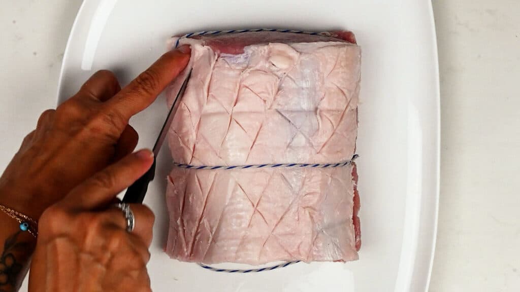 Scoring the fat layer of rolled pork loin using a knife