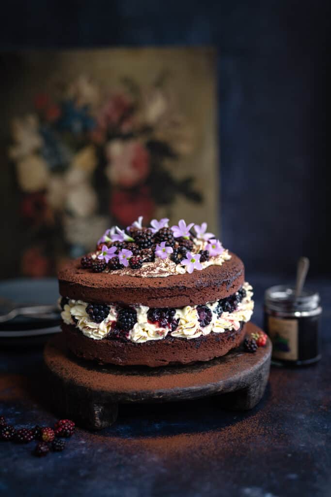 Chocolate Victoria Sponge with jam and whipped cream decorated with blackberries and flowers