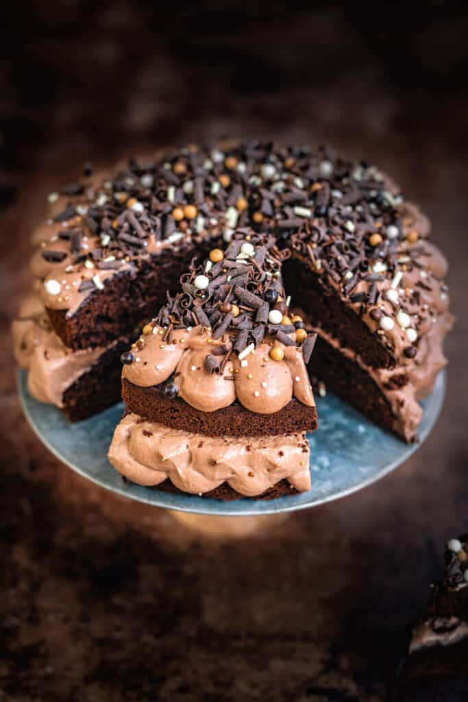 sliced chocolate Victoria sponge on a cake stand decorated with sprinkles and chocolate curls