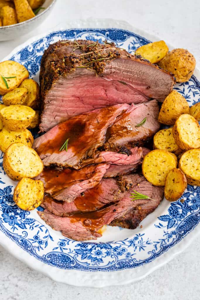 Sliced roast beef and gravy on a platter with roast potatoes