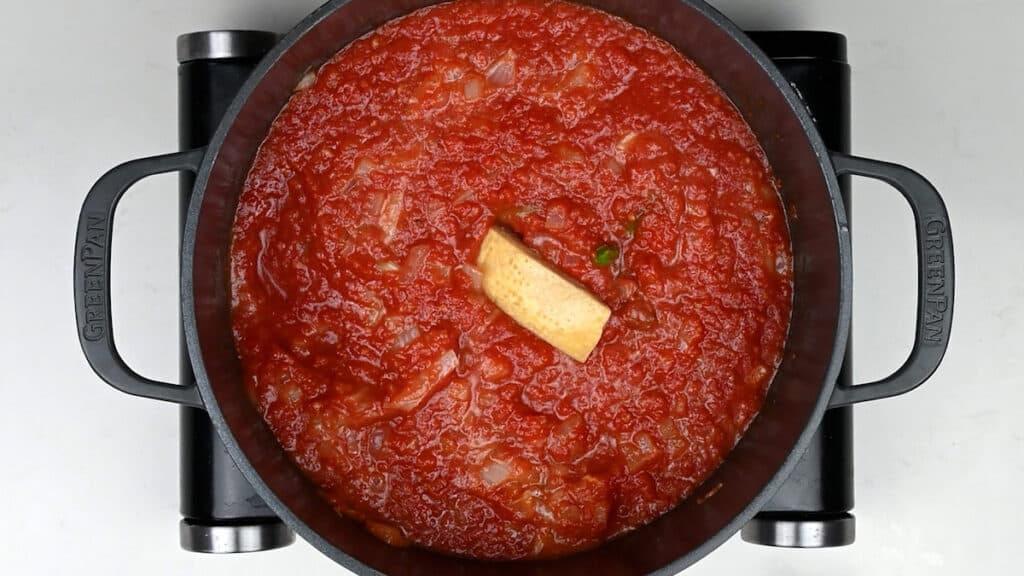 tomato sauce cooking in a pot with parmesan rind