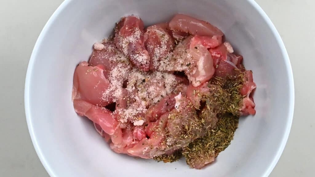 bowl of cubed chicken thighs with herbs and seasoning