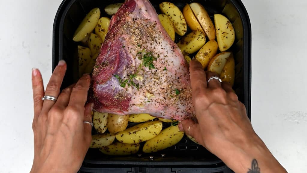 placing lamb in the air fryer over potatoes