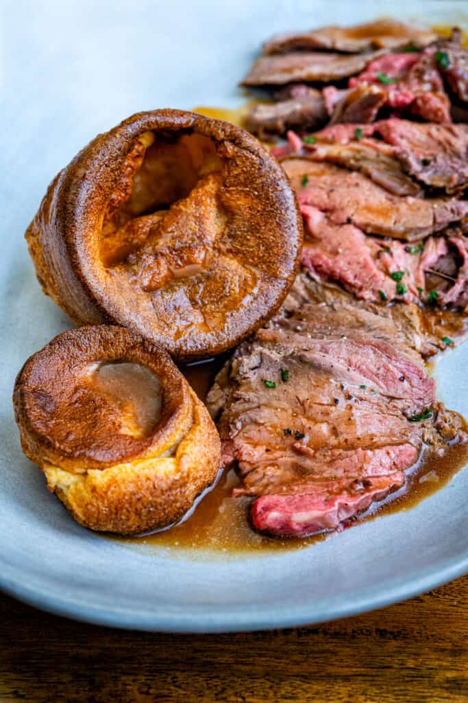 Sliced prime rib roast with gravy and Yorkshire puddings on a plate