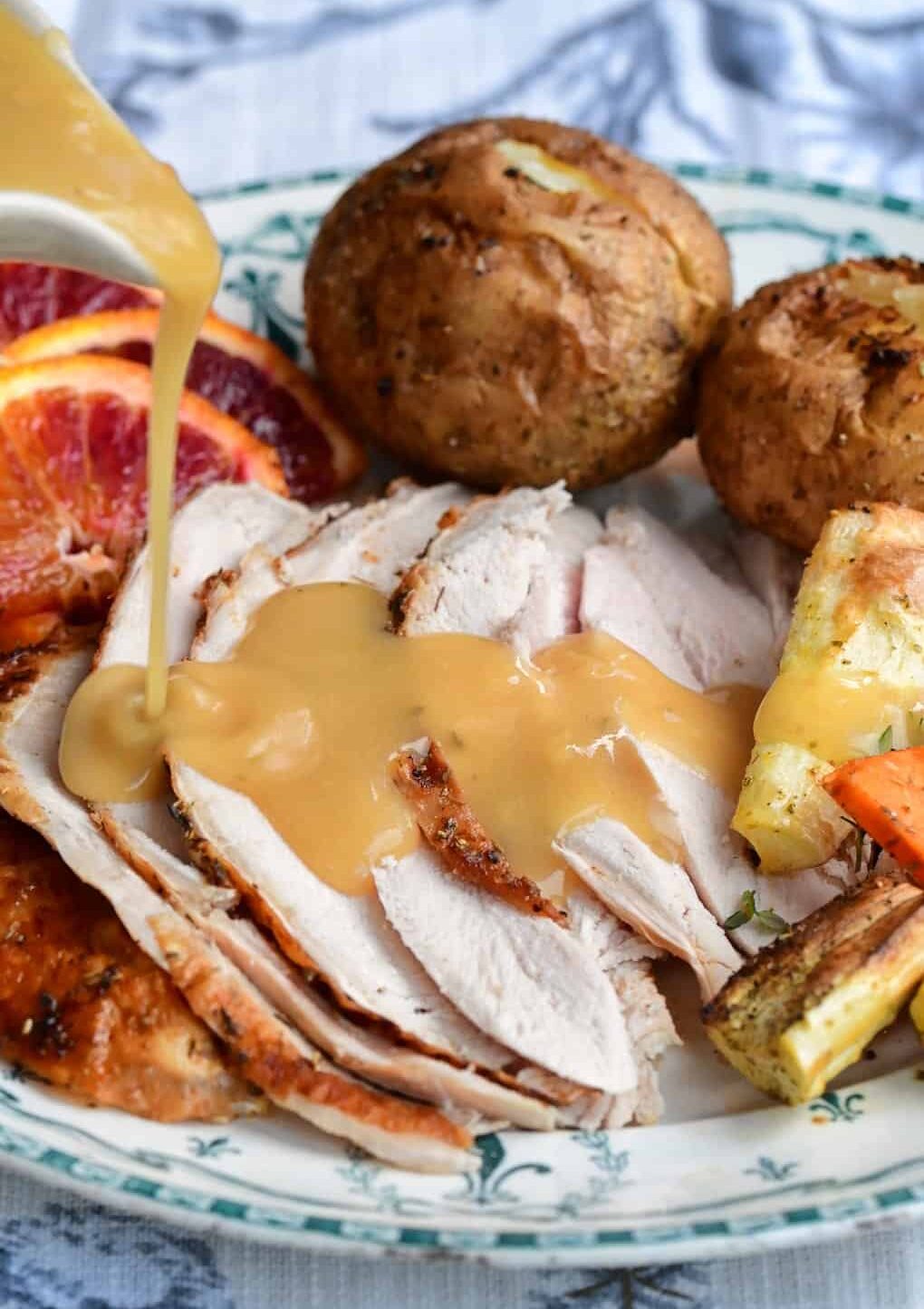 Air fryer turkey slices topped with gravy, served alongside roasted potatoes, vegetables, and orange slices on a decorative plate.