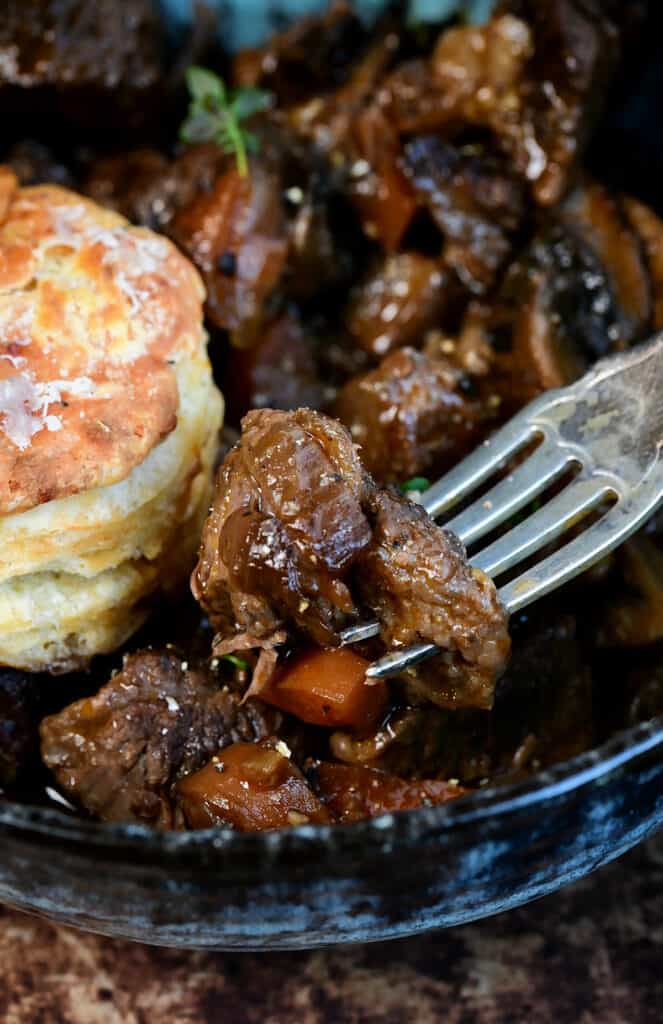 close up on beef stew in a bowl with cheese scone on the side