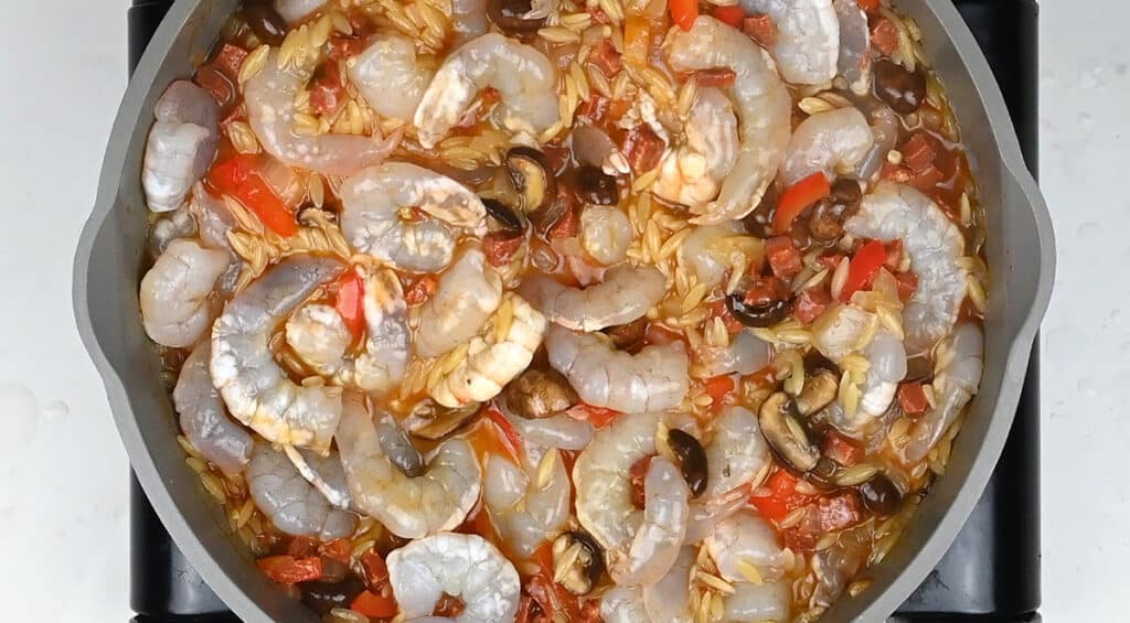 Shrimp cooking with orzo in a pan