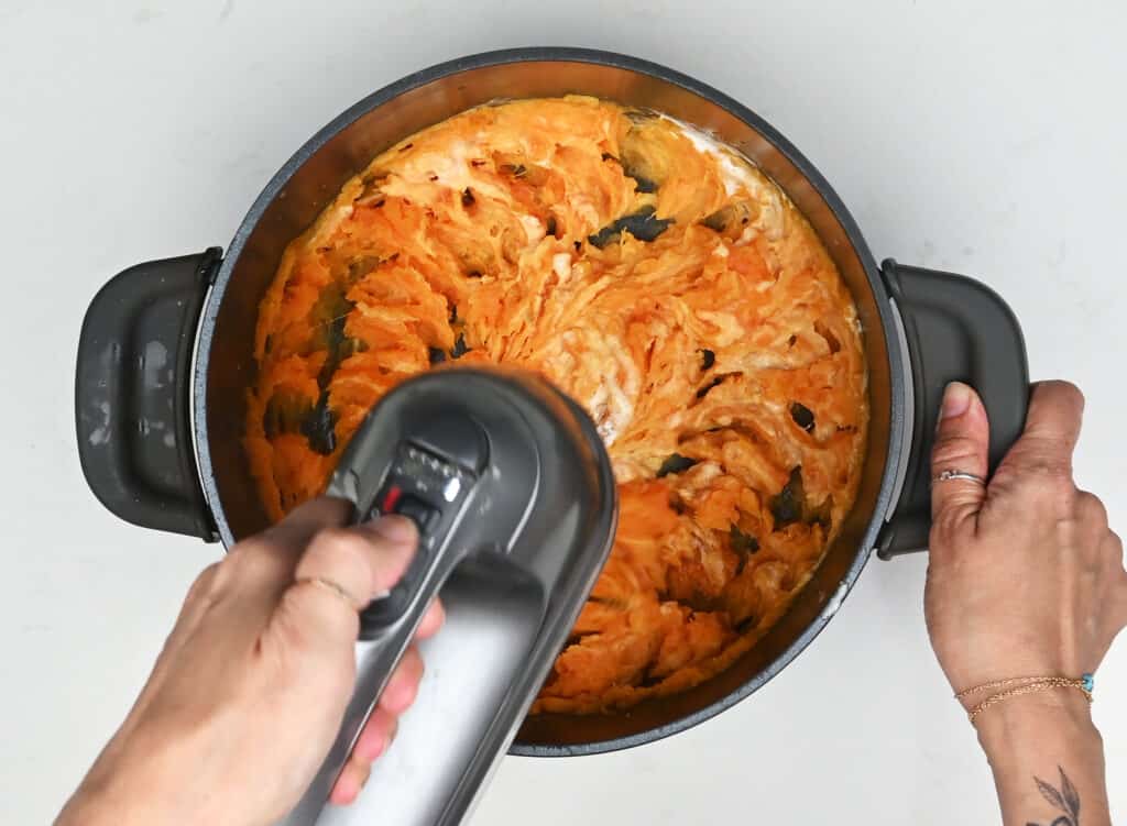 whipping sweet potatoes in a pot with an electric hand mixer