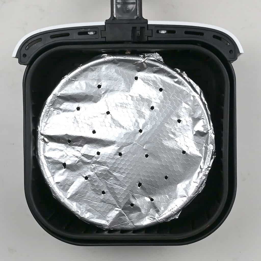 cake pan covered with foil in an air fryer basket