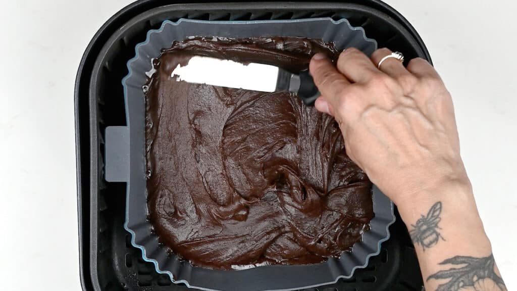 spooning brownie batter into a pan in an air fryer