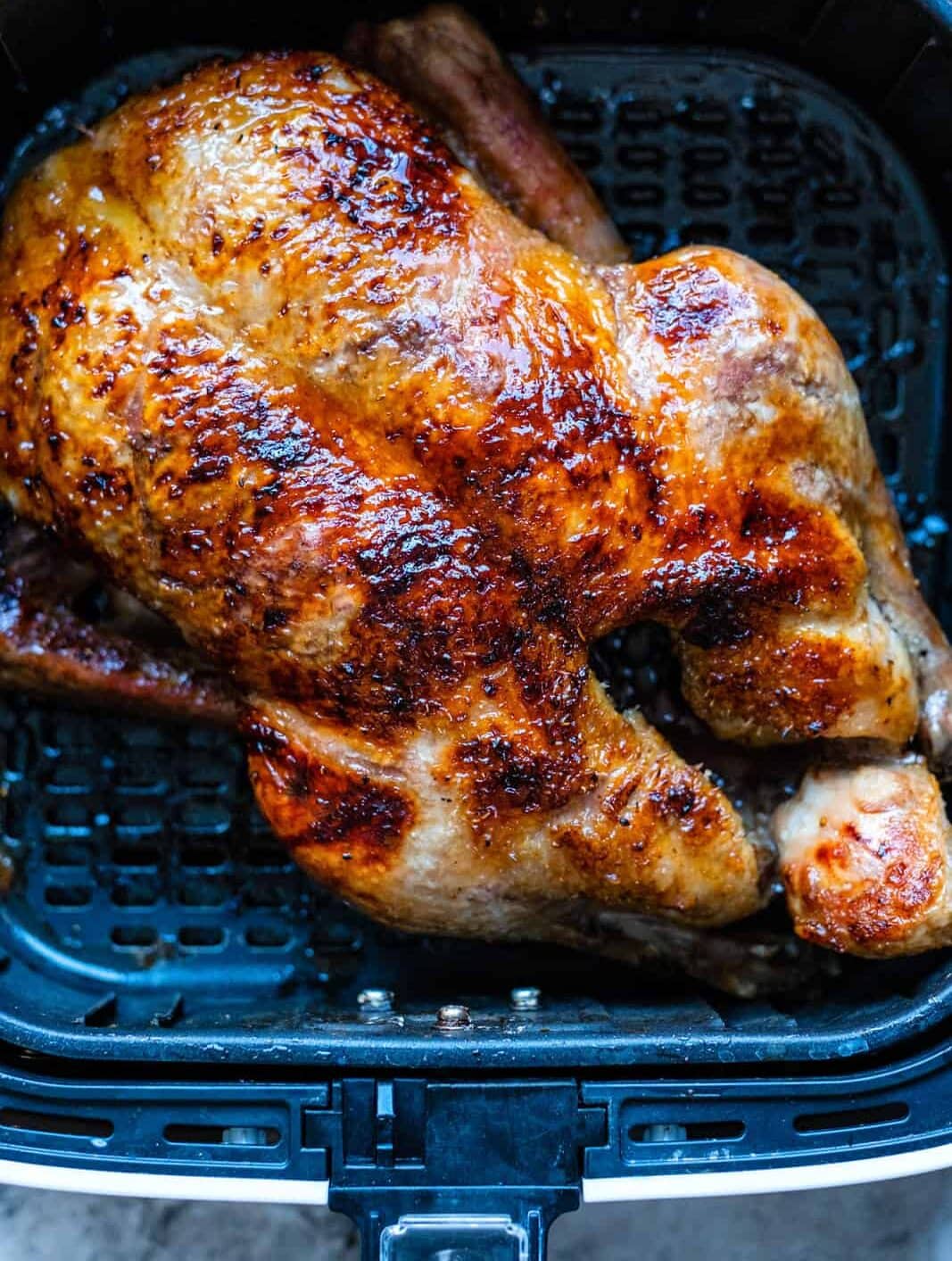 A whole roasted chicken with crispy, golden-brown skin sits in the basket of an air fryer, promising a meal as succulent and flavorful as any air fryer duck.