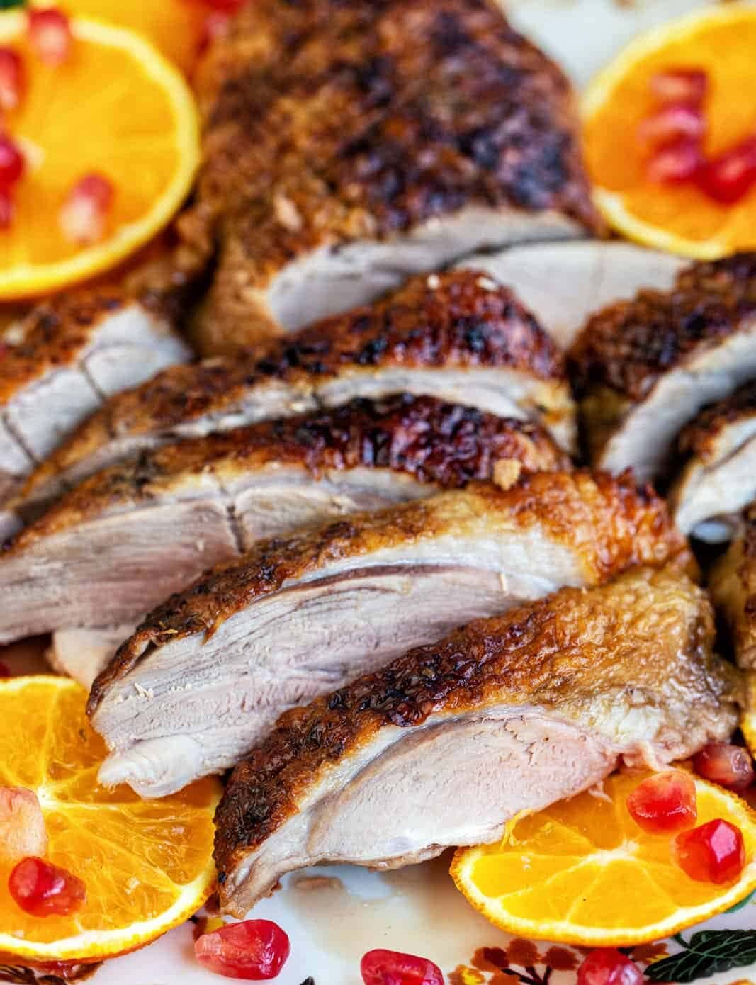 Air Fryer Duck breast with crispy skin, sliced and elegantly arranged on a platter, garnished with fresh orange slices and pomegranate seeds.