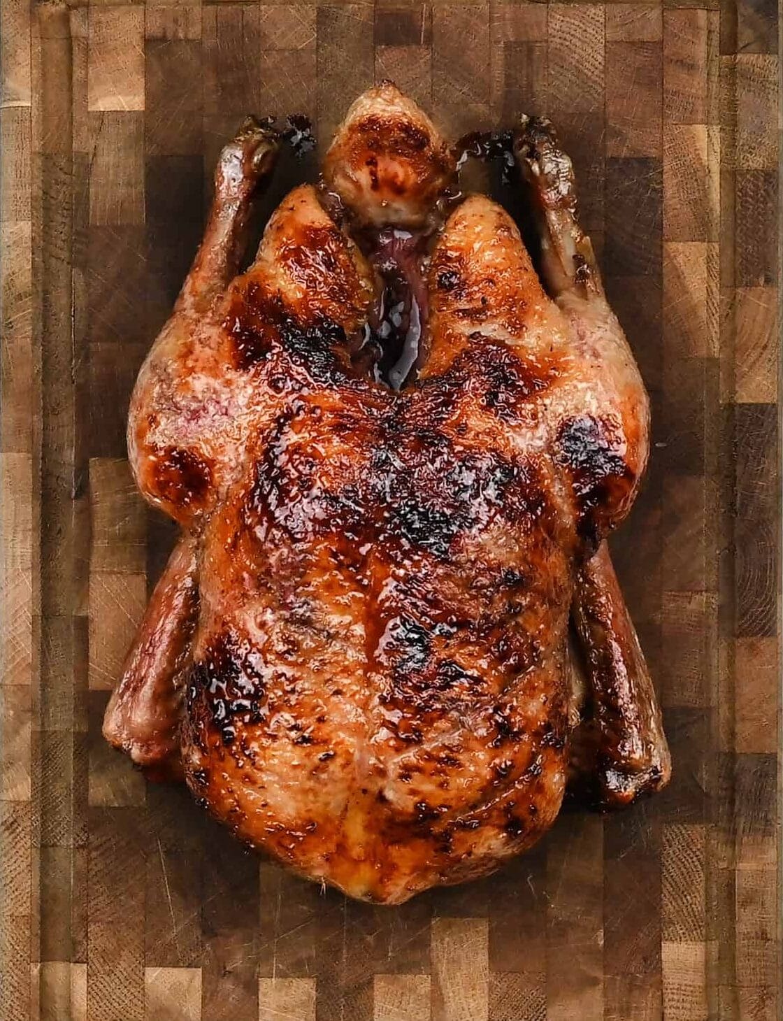 A whole Air Fryer Duck with crispy, golden-brown skin rests on a wooden cutting board, viewed from above.