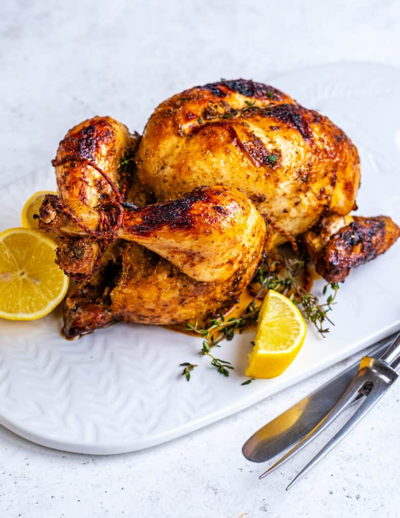 Rotisserie Chicken cooke in an air fryer on a plate with sliced lemon on the side