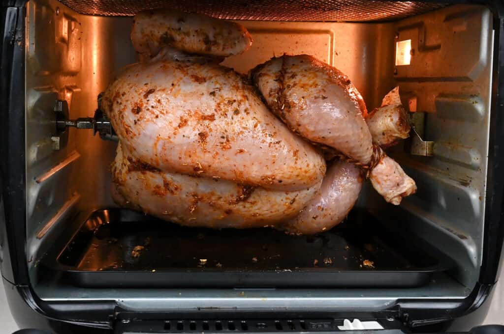 Chicken cooking on a rotisserie in an oven style air fryer