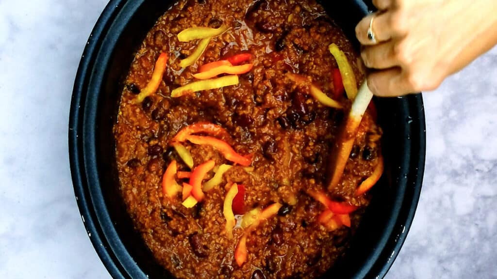 stirring sliced peppers into chilli in a slow cooker
