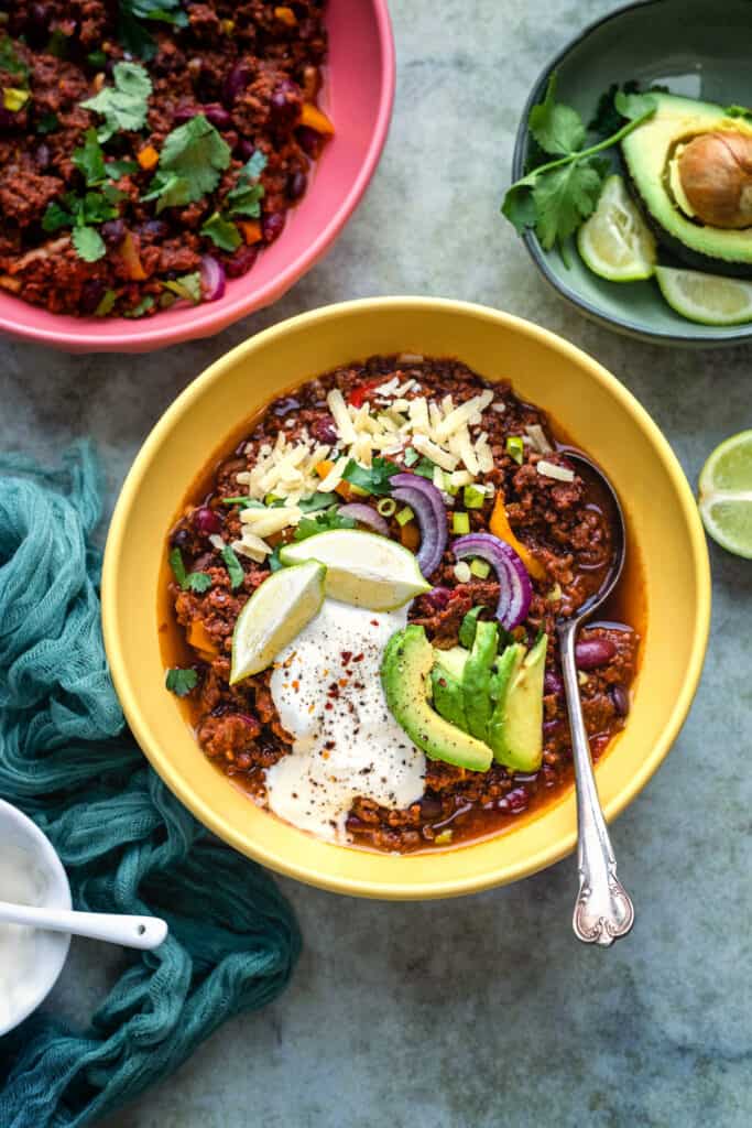 Bowl of chilli garnished with sour cream, avocado, grated cheese