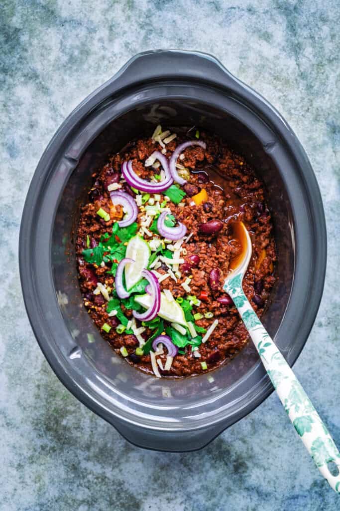 Slow cooker chilli con carne garnished with coriander, spring onions and lime wedges