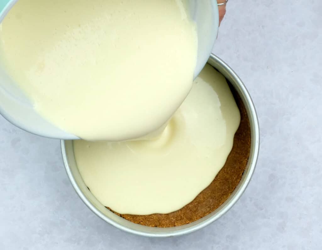 pouring cheesecake filling over crust