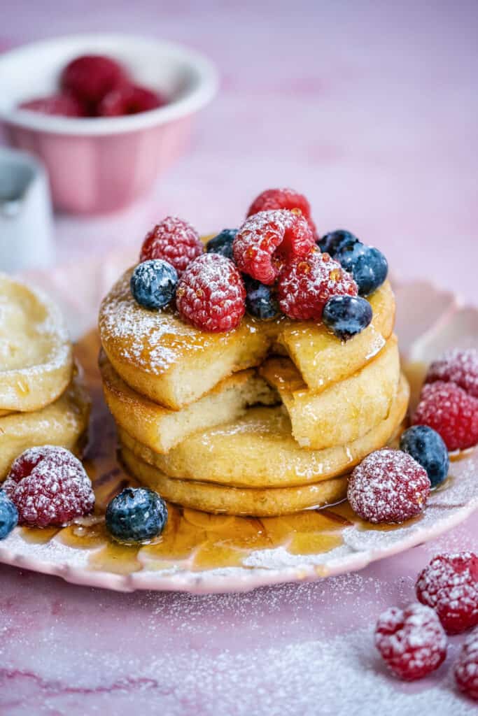 Three air fried pancakes on a pink plate with small slice cut out and berries on top