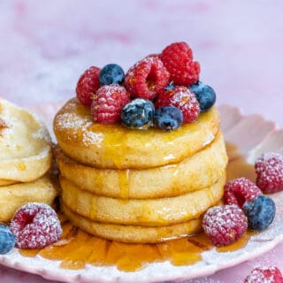 three fluffy air fried pancakes on a pink plate with syrup and berries