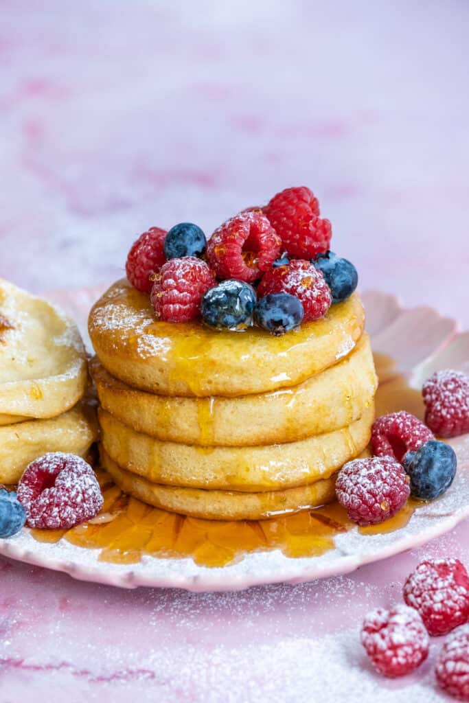 three fluffy air fried pancakes on a pink plate with syrup and berries
