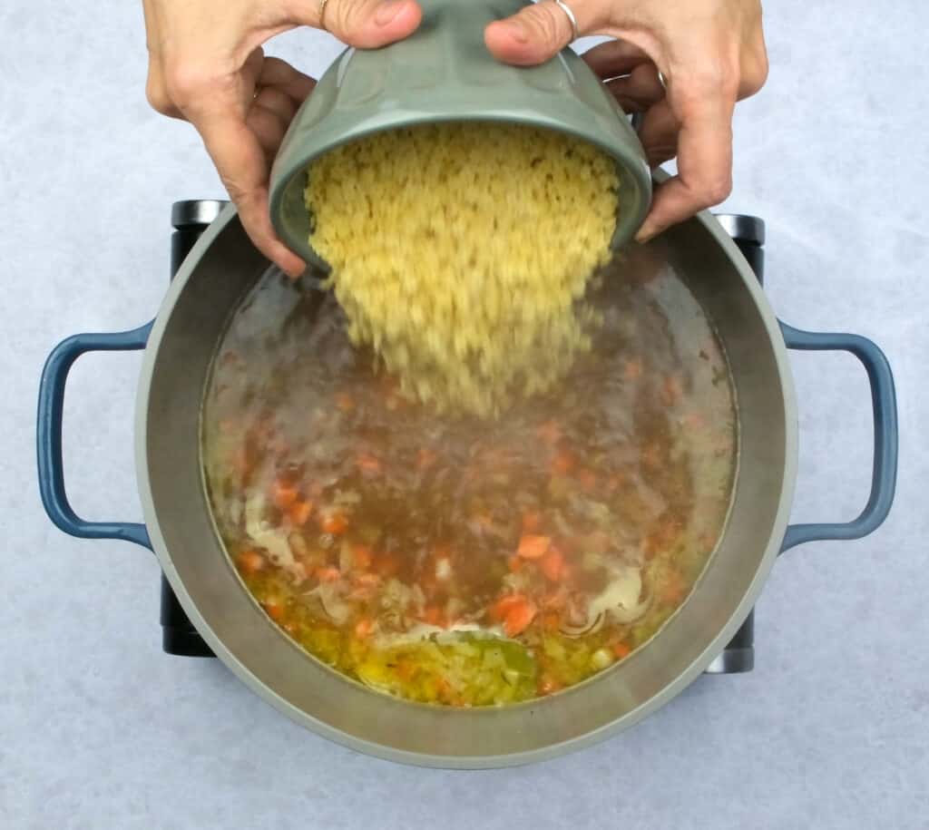 adding pastina to simmering chicken broth in a pot