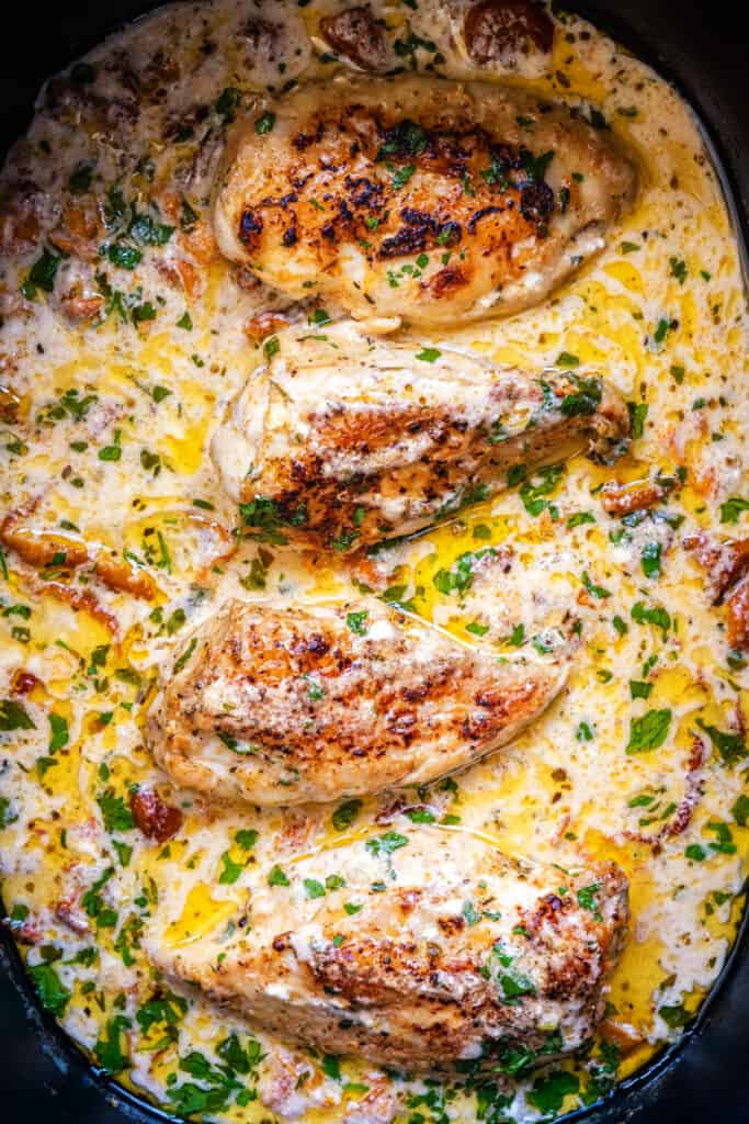 Close up on chicken breasts cooked in a creamy sauce in a crock pot