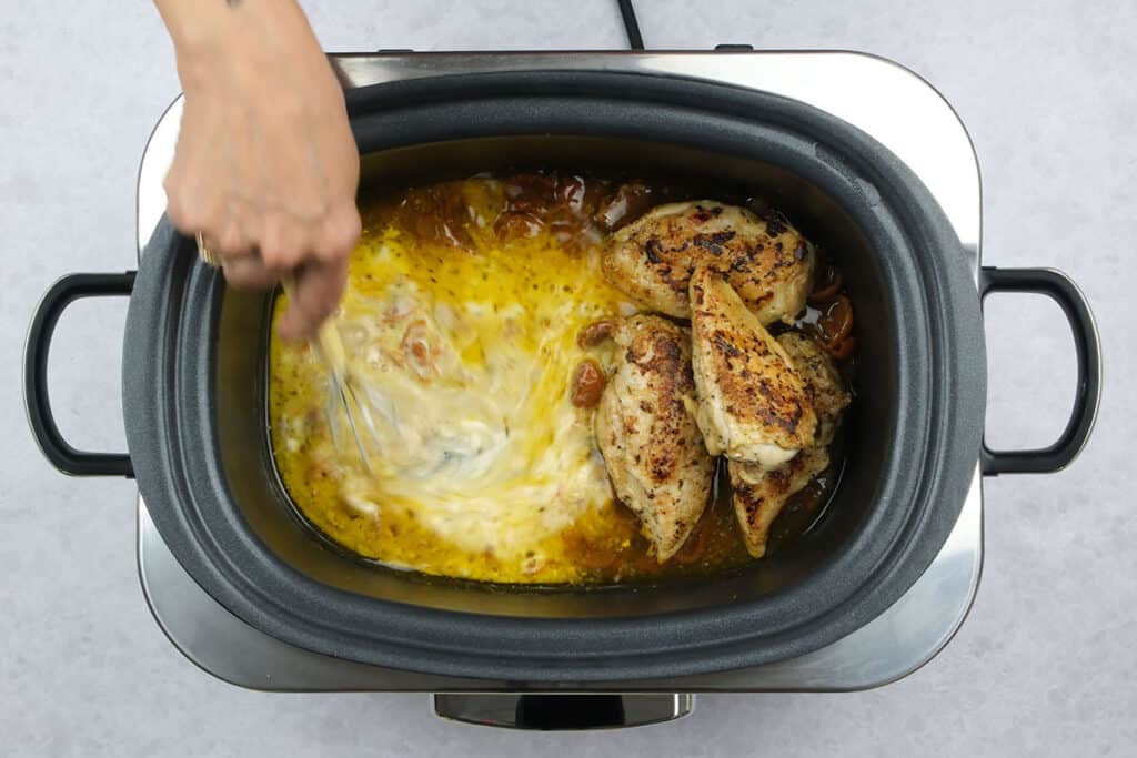 adding cream to chicken dish in a slow cooker