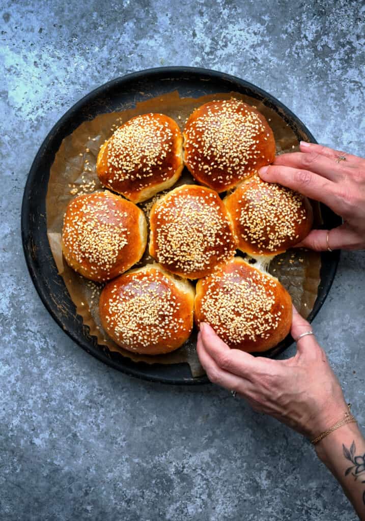 soft dinner rolls topped with sesame seeds, hands pulling one