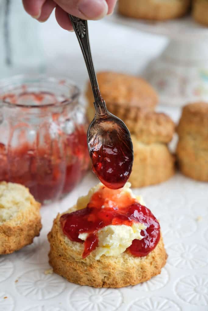 Adding jam to a scone topped with clotted cream