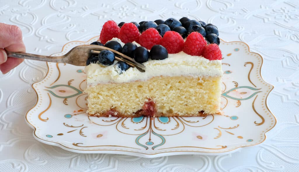 Slice of King Charles Coronation cake decorated with raspberries and blueberries on a plate