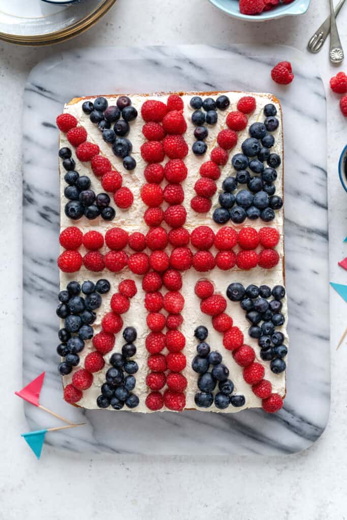 Coronation cake - sponge traybake spread with whipped cream and decorated with fresh berries to form a Union Jack