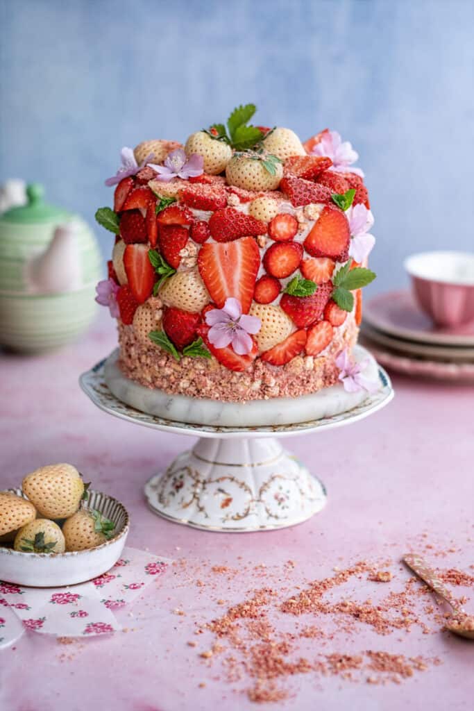 Strawberry crunch cake on a cake stand decorated with sliced strawberries