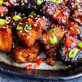 close up on a plate with sticky Air Fryerpork belly bites with sesame seed and spring onion garnish