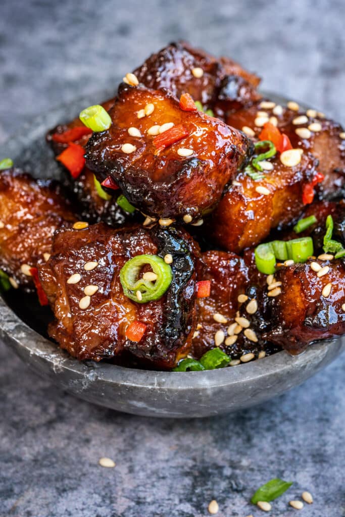 Crispy sticky Chinese style air fryer pork belly bites garnished with chilli, spring onion and sesame seeds in a small bowl