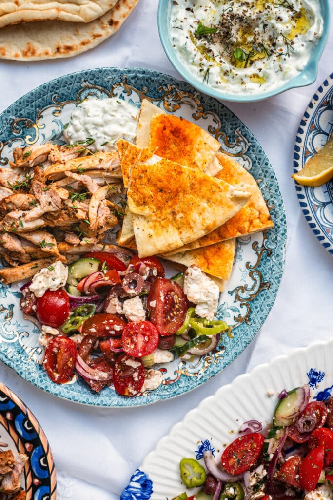 Air Fryer Greek chicken served sliced with Greek salad, pita bread and tzatziki on a patterned plate
