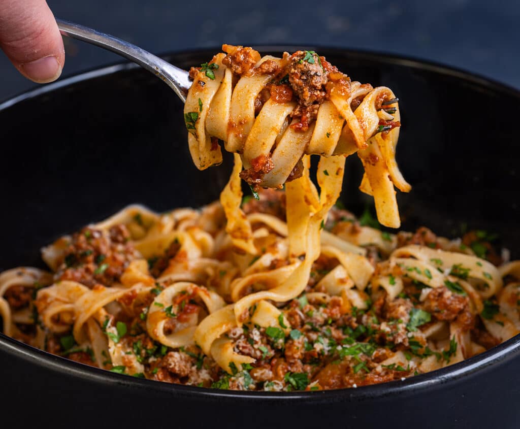 Fork holding up tagliatelle pasta with venison ragu