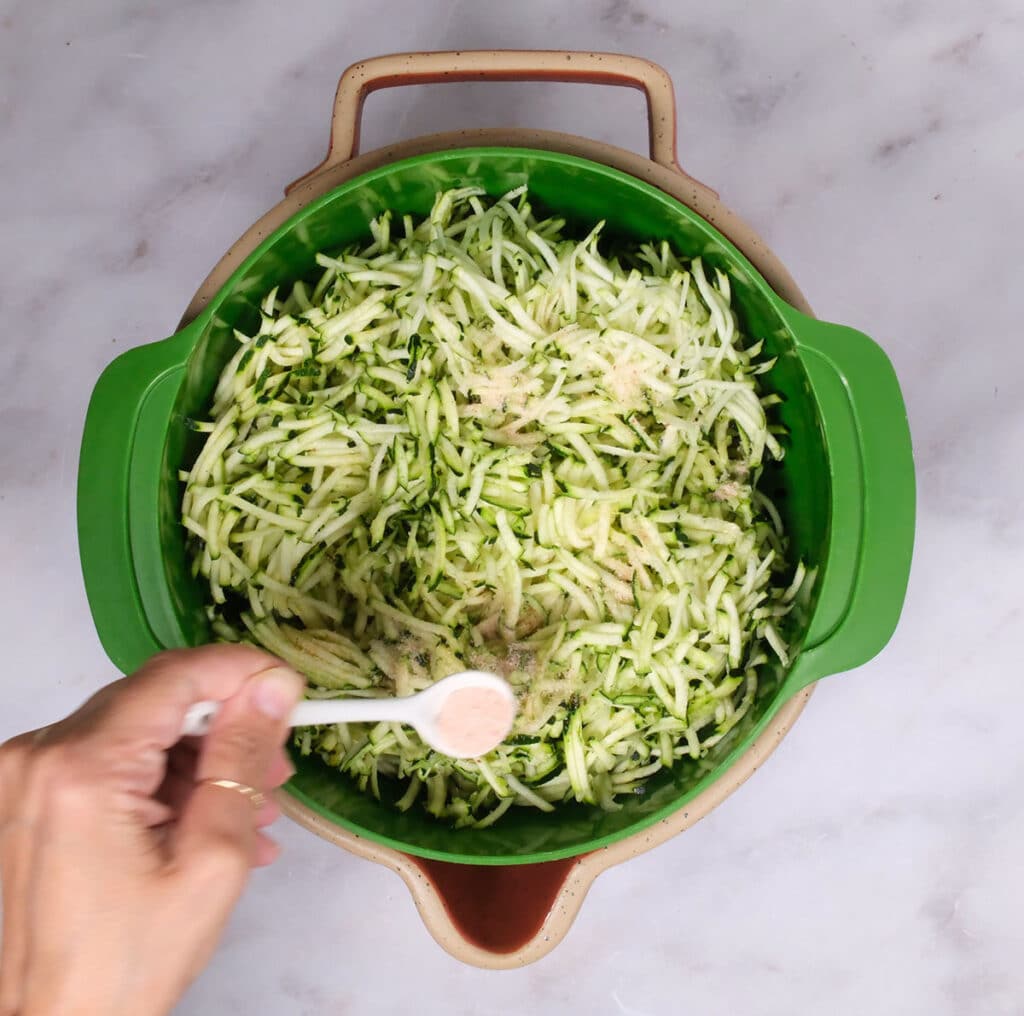 adding salt to a colander of grated zucchini