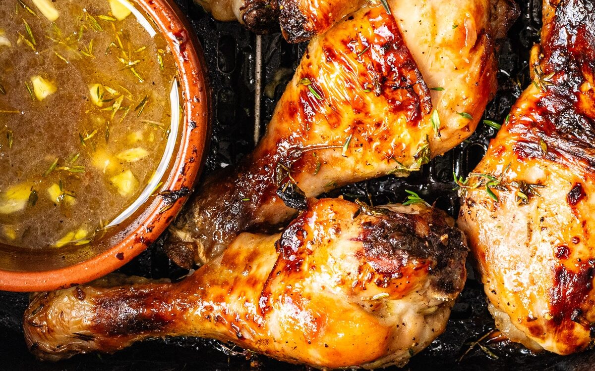 Close up on Air Fryer chicken drumsticks with a bowl of marinade on the side