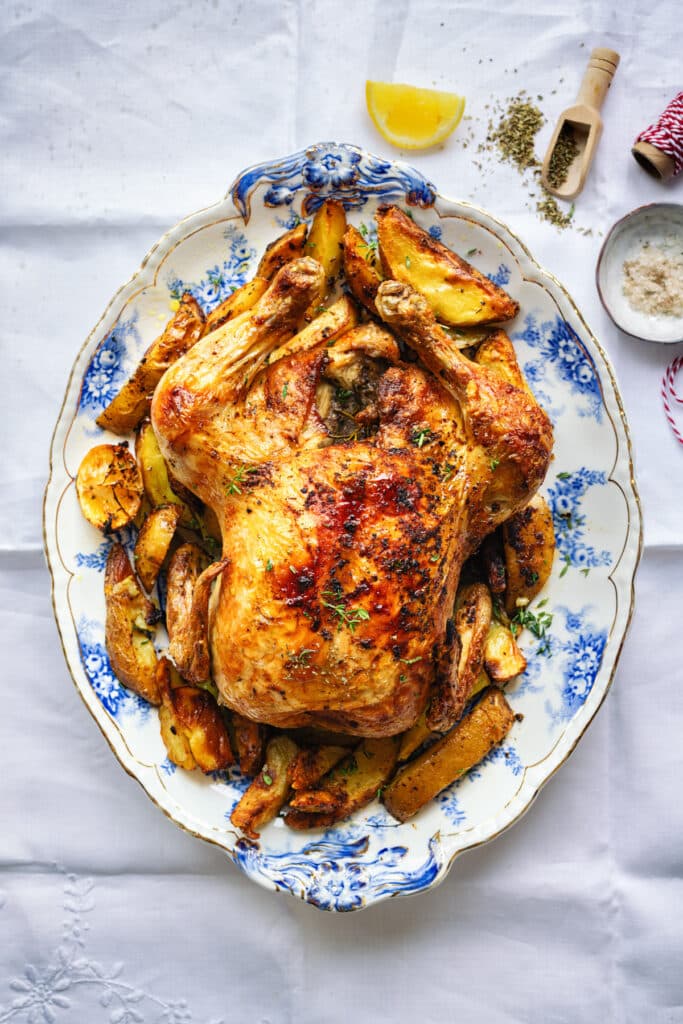Whole roast chicken cooked in an air fryer on a patterned plate with potato wedges