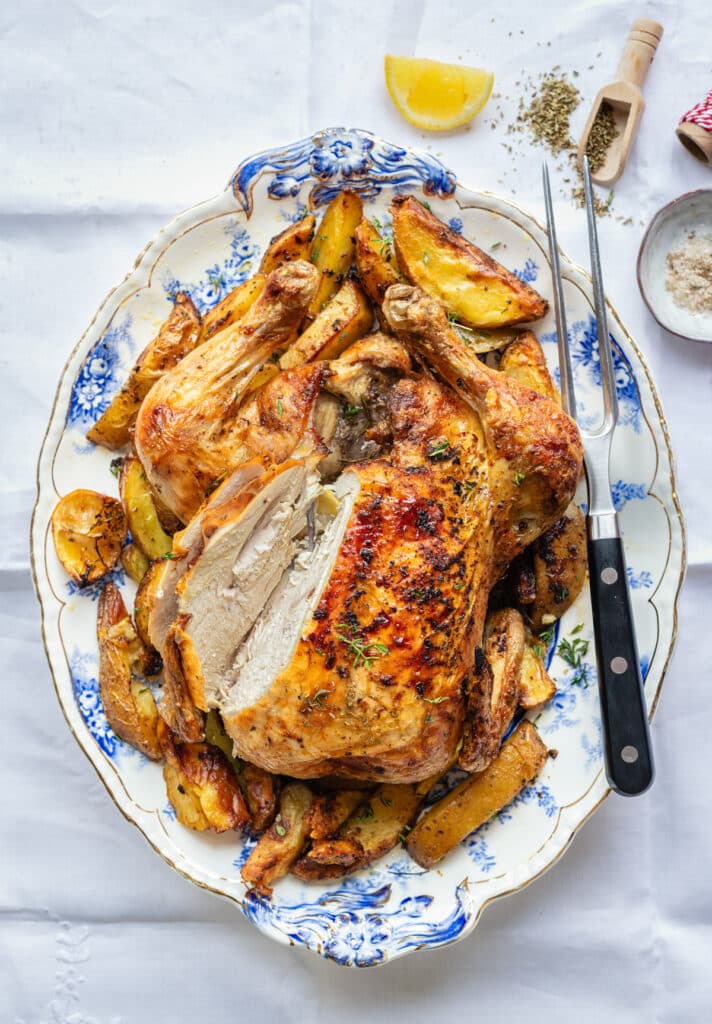Air Fryer Roast Chicken with lemon potatoes on a patterned platter with slice cut out