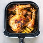 Air Fryer Whole Chicken shown in an air fryer basket with potato wedges