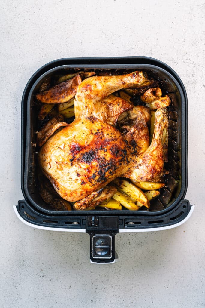 Air Fryer Whole Chicken shown in an air fryer basket with potato wedges